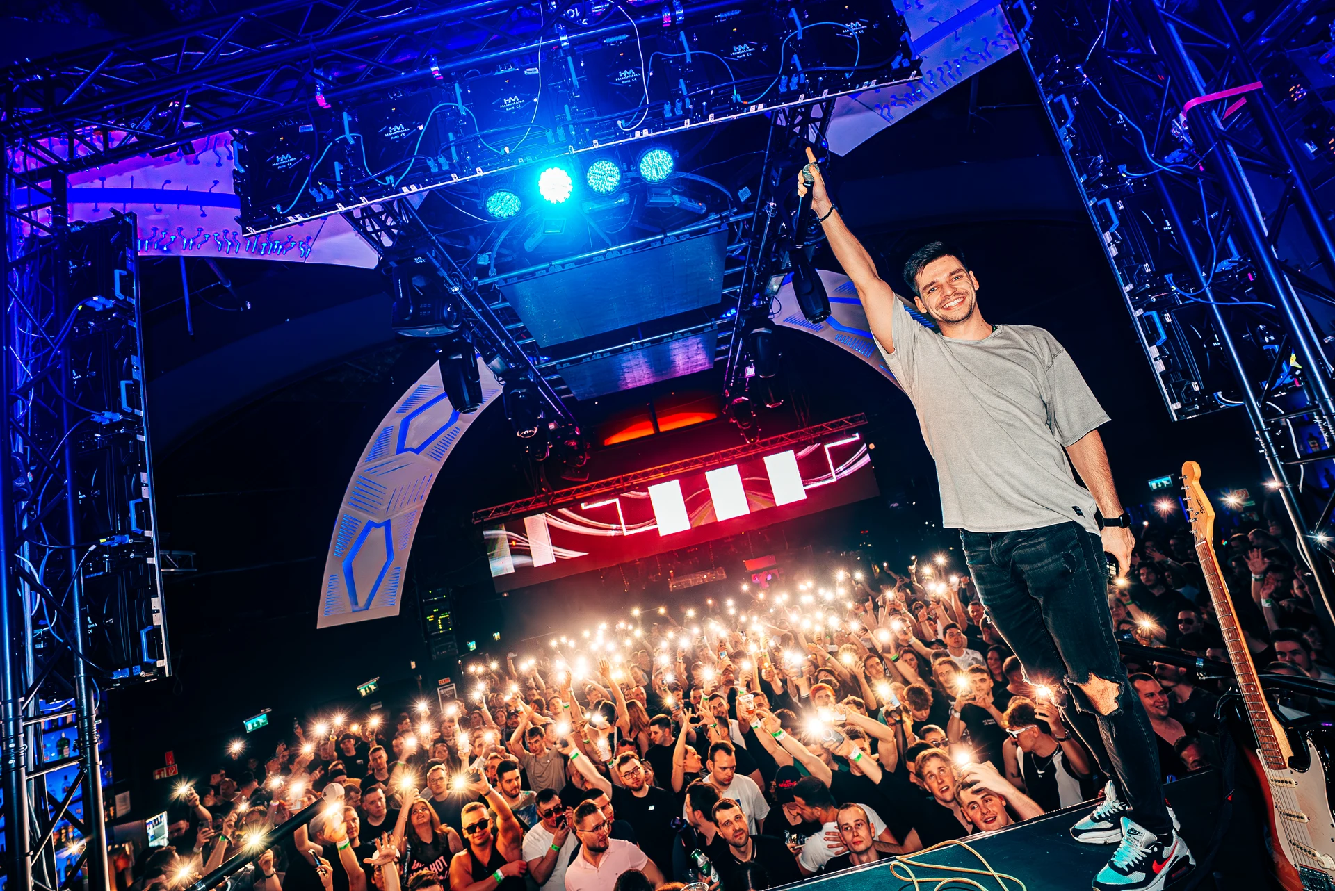 Subrage standing on the DJ booth in front of a phone-lit crowd